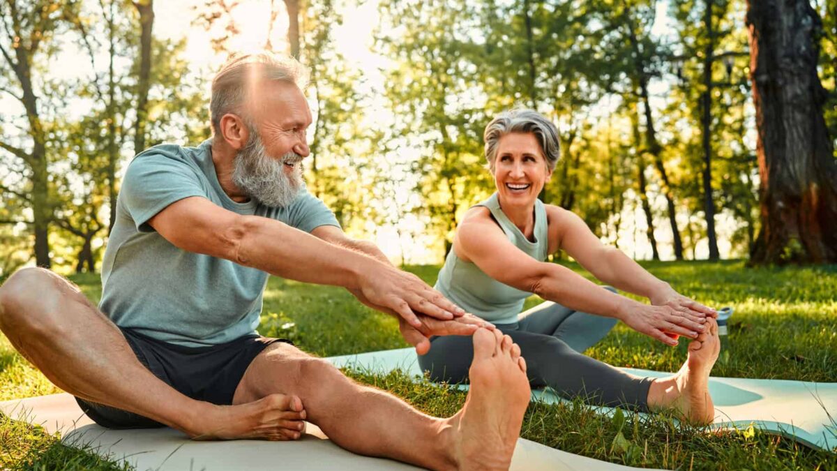 senior man and woman stretch their legs on yoga mats outside